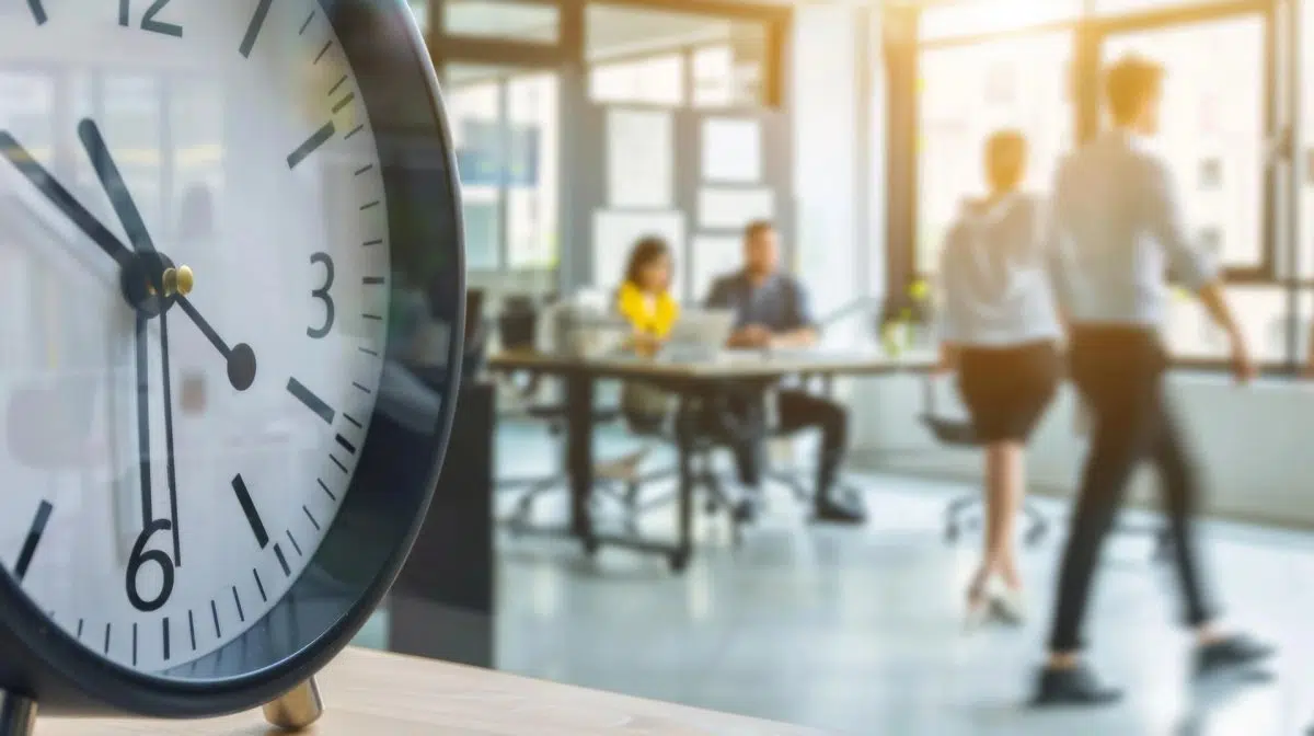 Reloj de pared frente a una oficina con personas trabajando